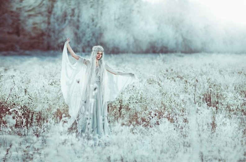 Белокурая фея с белой накидкой на плечах резвится в лесу
