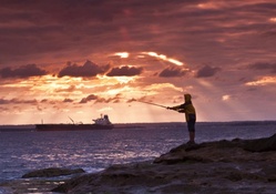 fisherman on a rocky bay shore at sunset