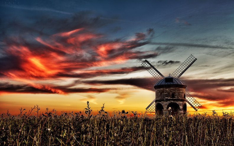 windmill in a field under fiery skies