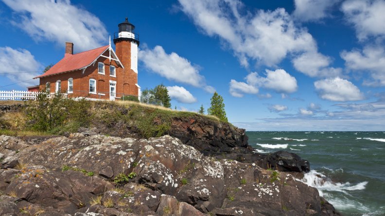 red brick lighthouse on a cliff overlooking the sea