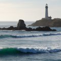 lighthouse above turqoise waves on a rocky beach
