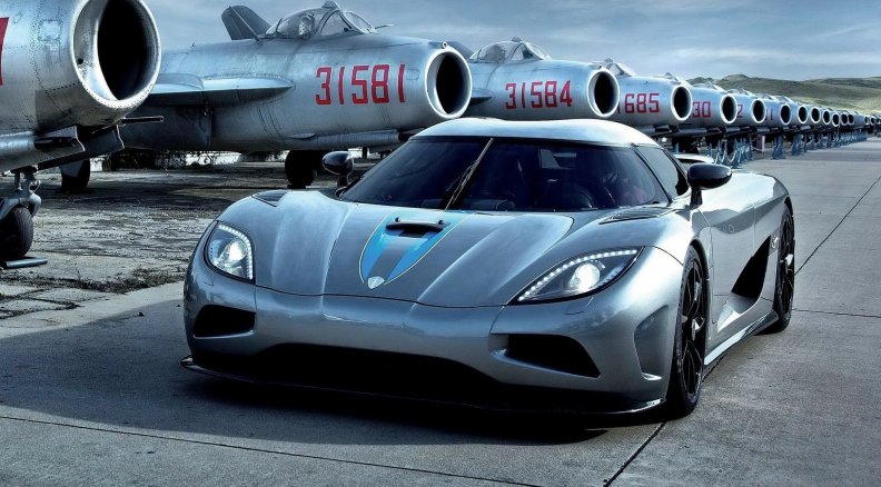 koenigsegg at an airport of old mig planes