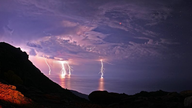 lightning storm off coast on a starry night