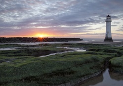 sunset on a lighthouse past a marsh