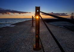 sunset through a metal post on a pier