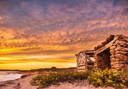stone and wooden huts on a beach at sunset