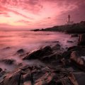 fantastic pink sunset over lighthouse on rocky shore